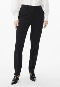 Black tailored trousers with a slim fit, featuring smooth fabric, angled pockets, and subtle front crease lines, complemented by pointed black heels.