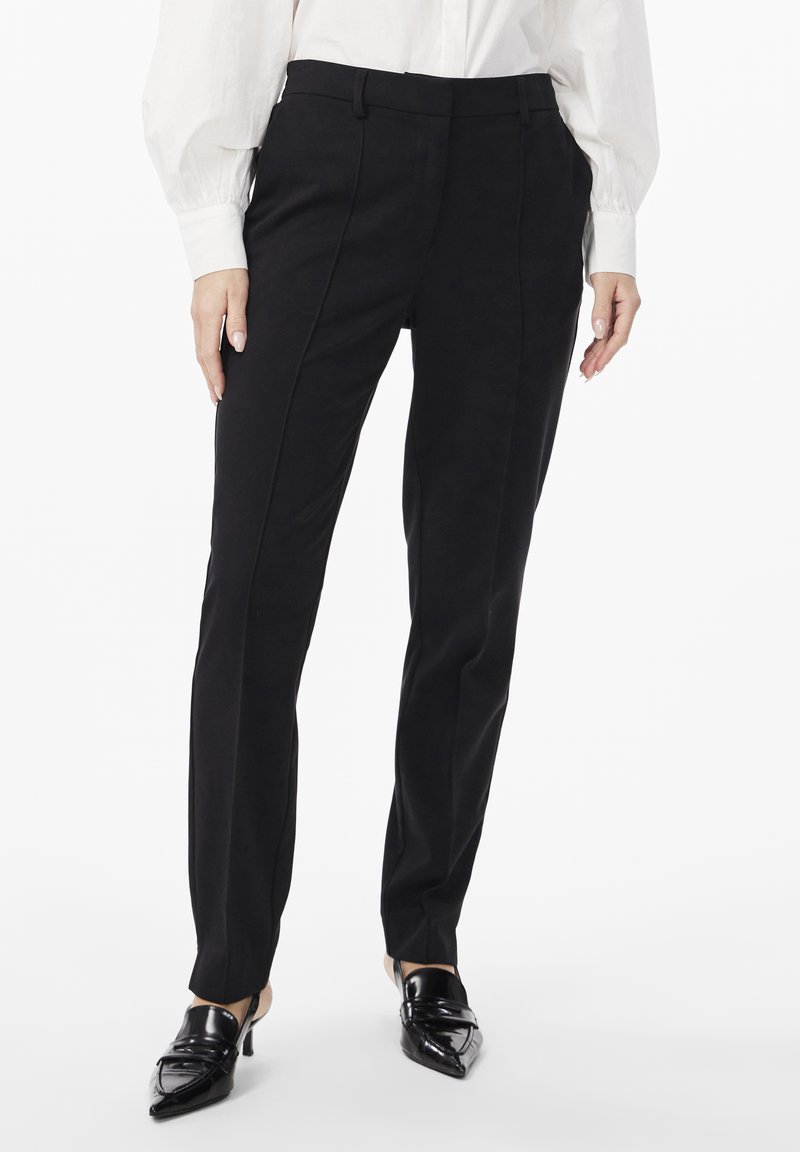 Black tailored trousers with a slim fit, featuring smooth fabric, angled pockets, and subtle front crease lines, complemented by pointed black heels.
