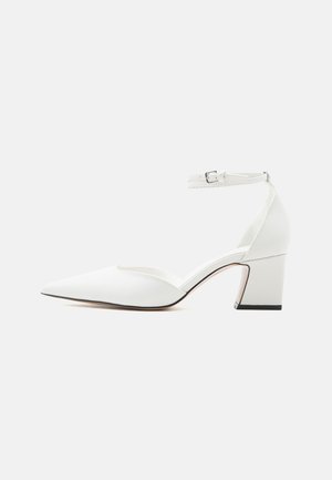 Weißer Schuh mit spitz zulaufender Vorderkappe, mittelhohem Absatz, Knöchelriemen und Schnalle, glatter Oberfläche und Blockabsatz vor einfachem, hellem Hintergrund.