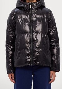 Veste noire matelassée avec finition brillante, dotée d'une capuche, d'une fermeture éclair devant et de poches plaquées. Légère avec une texture matelassée visible.