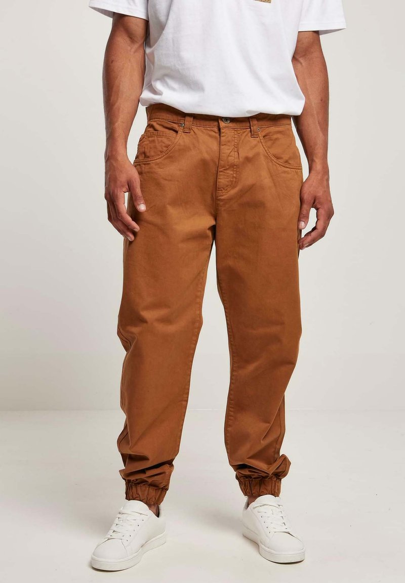Brune bomulds joggerbukser med elastiske manchetter, der har sidelommer og en afslappet pasform, parret med hvide sneakers.