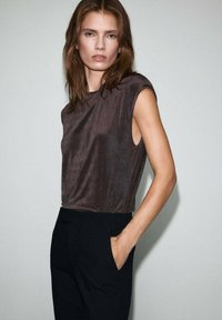 Hnedý bezrukávový top s hladkou textúrou a voľným strihom, kombinovaný s čiernymi, strihanými nohavicami s bočnými vreckami.