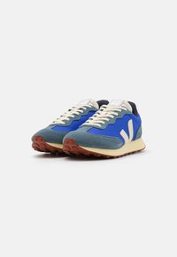 Blue mesh and suede sneakers feature a cream sole, beige laces, and a red and navy accent on the heel, with textured rubber outsole.