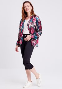 Kimono-Jacke mit Blumenmuster in lebendigen Farben, leichtes Material, lockere Passform, kombiniert mit schwarzen, kurz geschnittenen Leggings und weißen Sneakern.