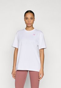 Bijela majica od pamuka s kratkim rukavima, okruglim izrezom i malim ružičastim logotipom na lijevoj strani. Glatka tekstura, ležerni kroj.