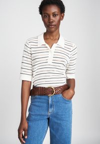 Cream polo shirt with black stripes and perforated pattern, paired with blue denim jeans and a brown woven belt featuring a circular buckle.