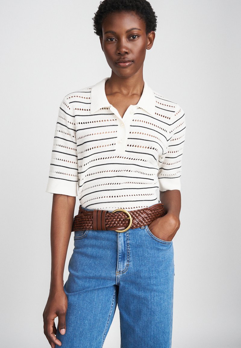 Cream polo shirt with black stripes and perforated pattern, paired with blue denim jeans and a brown woven belt featuring a circular buckle.
