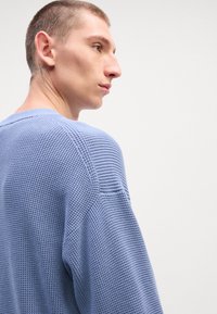 Sweater azul claro texturizado com um corte solto, apresentando um decote redondo e acabamentos canelados na gola e nas mangas.