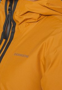 Vandafvisende orange jakke med hætte, der har sort lynlås og snore, glat tekstur og diskret logo.