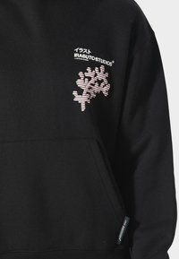 Zwarte sweatshirt met een roze grafiek van in elkaar gewoven lijnen op de borst. Inclusief merktekst "IRASUTOSTUDIOS" boven de grafiek.