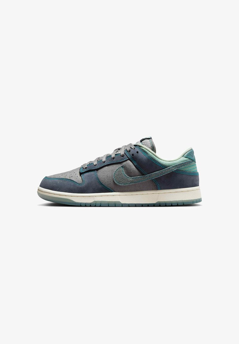 Låg Nike-sneaker i grått och teal med textil- och mockapaneler, snören och vit sula.