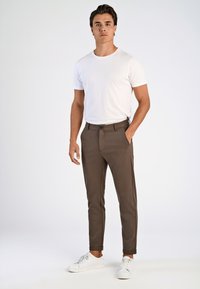 Bruine slim-fit broek met voorzakken, een vlakke voorkant en een enkele knoopsluiting. Gecombineerd met een witte crewneck t-shirt en witte sneakers.