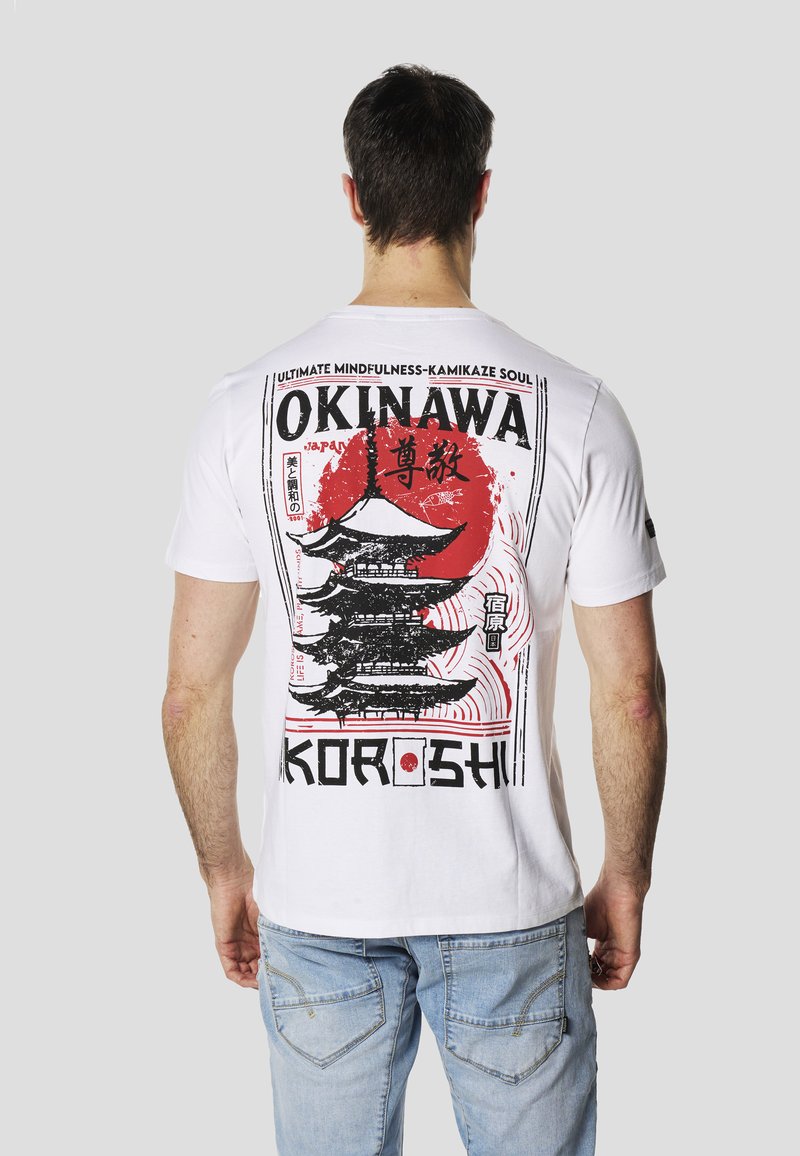 T-shirt bianca a maniche corte con stampa grafica di una pagoda e un cerchio rosso. Testo include "Okinawa" e "Koroshi", con accenti neri.