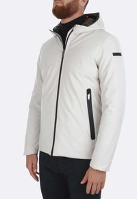 Giacca impermeabile bianca con cappuccio, tasche zippate nere e fodera interna a contrasto. Presenta un design elegante e moderno con una texture liscia.