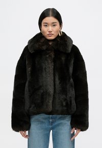 Σκοτεινό τζάκετ από συνθετική γούνα με φαρδύ γιακά, χαλαρή γραμμή και μαλακή υφή. Διαθέτει μακριά μανίκια και συνδυάζεται με ανοιχτό μπλε τζιν.