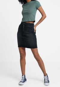 Mörk denim blyertsskjorta med rå kant, framknäppning och fem fickor, tillsammans med en kort grön ribbad topp och blå högsneakers.