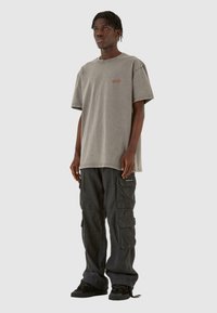 Grå oversized t-shirt med et subtilt logo på brystet, parret med mørke cargo-bukser med flere lommer og en tekstureret finish.
