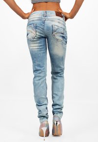 Jeans skinny blu con un lavaggio sbiadito, design a cinque tasche, cuciture dettagliate e tasche posteriori decorative, abbinati a tacchi alti iridescenti.