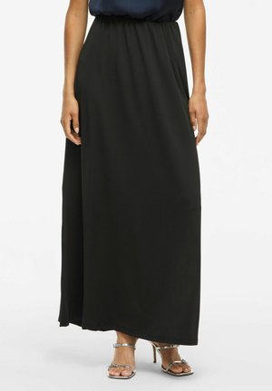 Jupe maxi noire avec une taille élastique, texture lisse, design fluide et coupe droite, associée à des talons aiguilles argentés.