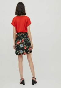 Haut rouge à manches courtes associé à une jupe noire à motifs floraux comportant des fleurs colorées et une taille élastique. Sandales à talons carrés noires.