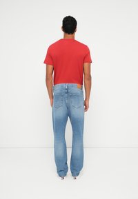 Κόκκινο κοντομάνικο πουκάμισο και ανοιχτό μπλε τζιν με ίσια γραμμή και ξεθωριασμένη υφή. Τα τζιν έχουν καφέ ετικέτα και δύο πίσω τσέπες.