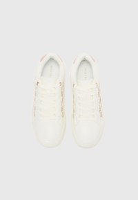Scarpe da ginnastica bianche con accenti rosa chiaro, caratterizzate da un design con lacci e un motivo decorativo in tonalità oro sui lati. Texture liscia e forma arrotondata.