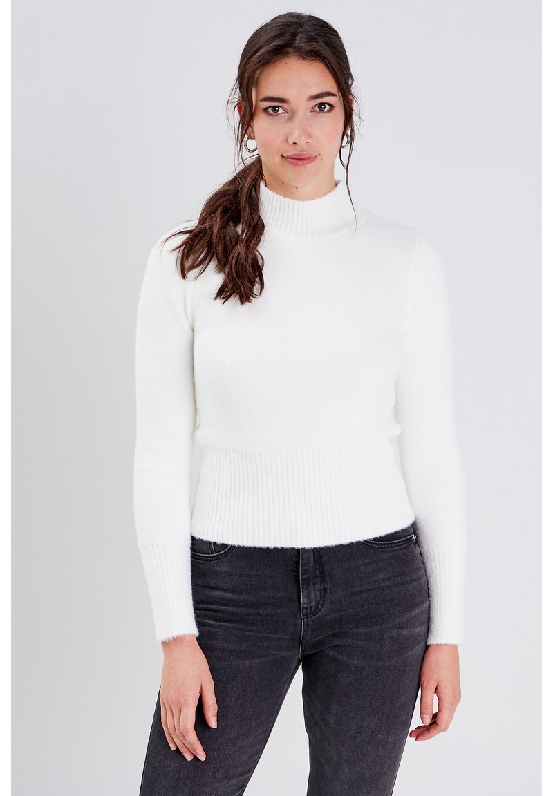 Pull col roulé blanc avec une texture douce et duveteuse et un ourlet côtelé, associé à un jean sombre. Design minimaliste, sans motifs ni embellissements.