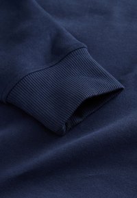 Manžeta tamnoplave majice s rebrastom teksturom. Tkanina izgleda mekano, s glatkim završetkom i suptilnom rastezljivošću.