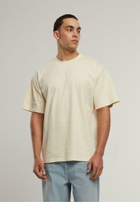 Šviesiai geltona trumpomis rankovėmis marškinėliai su subtiliu raštu, apvalia kaklo iškirpte ir laisvu kirpimu. Audinys atrodo minkštas su lygia tekstūra.