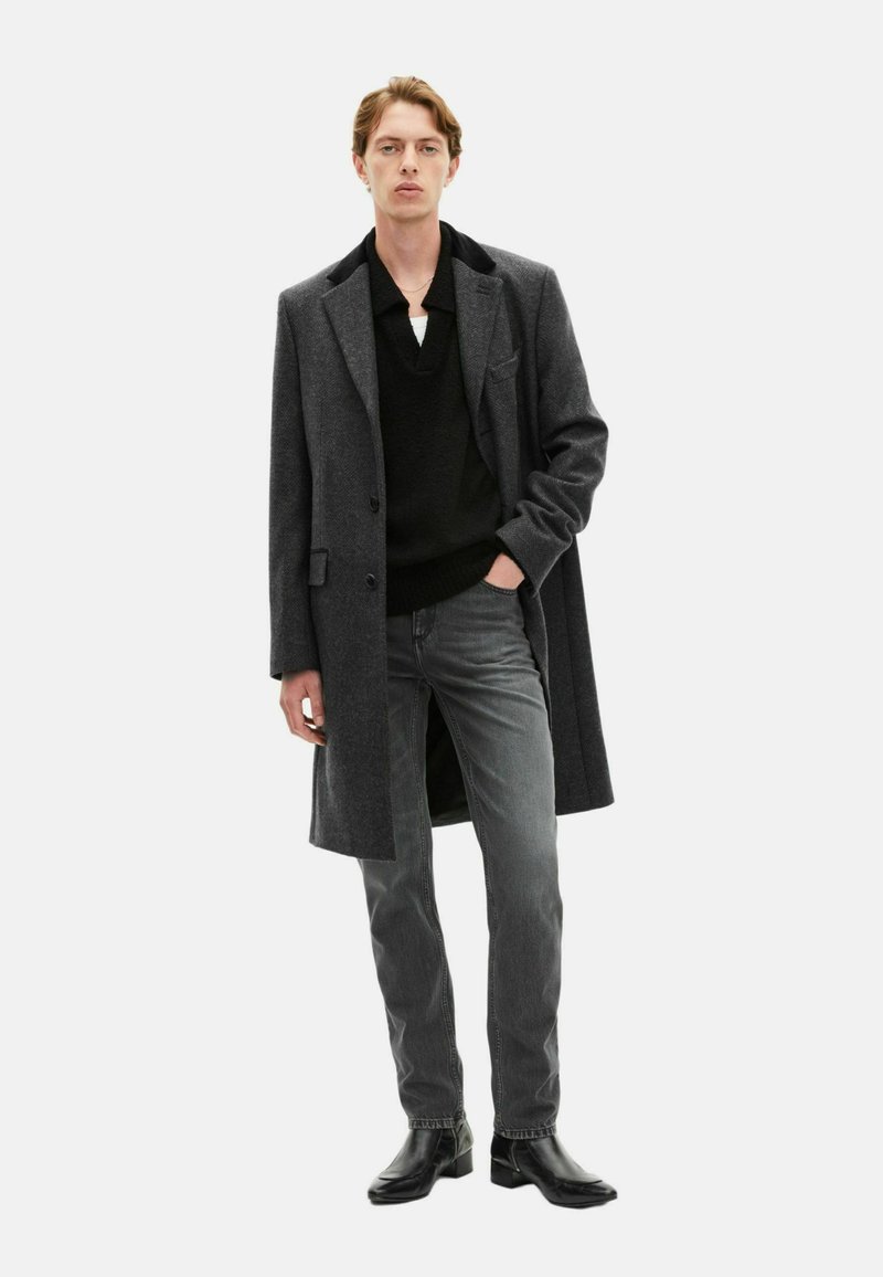 Charcoal gray wool blend overcoat with notch lapels, layered over a black knit sweater, paired with gray jeans and black leather boots.