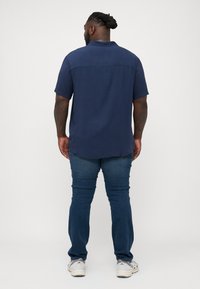 Camisa de botones marinera con mangas cortas, un ajuste relajado y una textura suave, combinada con jeans azules y zapatillas grises.