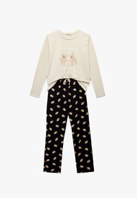 Langærmet cremefarvet top med teddy bear-print og tekst, parret med sorte bukser med gentagne teddy bear-mønstre. Blødt bomuldsstof hele vejen igennem.