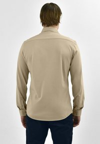 Beige blouse met lange mouwen en een puntige kraag, knoopmanchetten en een gladde textuur, gedragen met donkere broek, vanuit de rug gezien.