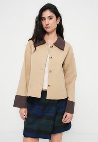 Μπεζ κομμένο σακάκι με καφέ ριμπ γιακά και μανσέτες, διακοσμημένο με μεγάλα κουμπιά. Συνδυασμένο με μπλε και μαύρη καρό φούστα.