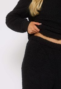 Ensemble de loungewear en polaire noire avec une finition texturée et duveteuse. Le haut a des manches longues et un ourlet court, assorti à un pantalon à taille élastique.