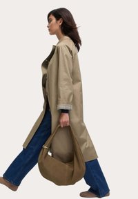 Beige trenchcoat met een losse pasvorm, knoopdetails en lange mouwen, gecombineerd met blauwe jeans en een bruine stoffen handtas.