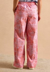 Rosa, leichte Stoffhosen mit einem malerischen orangen Druck, der Segelboote und Palmen zeigt. Elastischer Bund, lockere Passform und Seitentaschen.