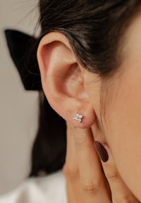 Orecchino a bottone in argento a forma di stella, adornato con piccole pietre preziose trasparenti. Vista ravvicinata vicino a un orecchio, con capelli scuri sullo sfondo.