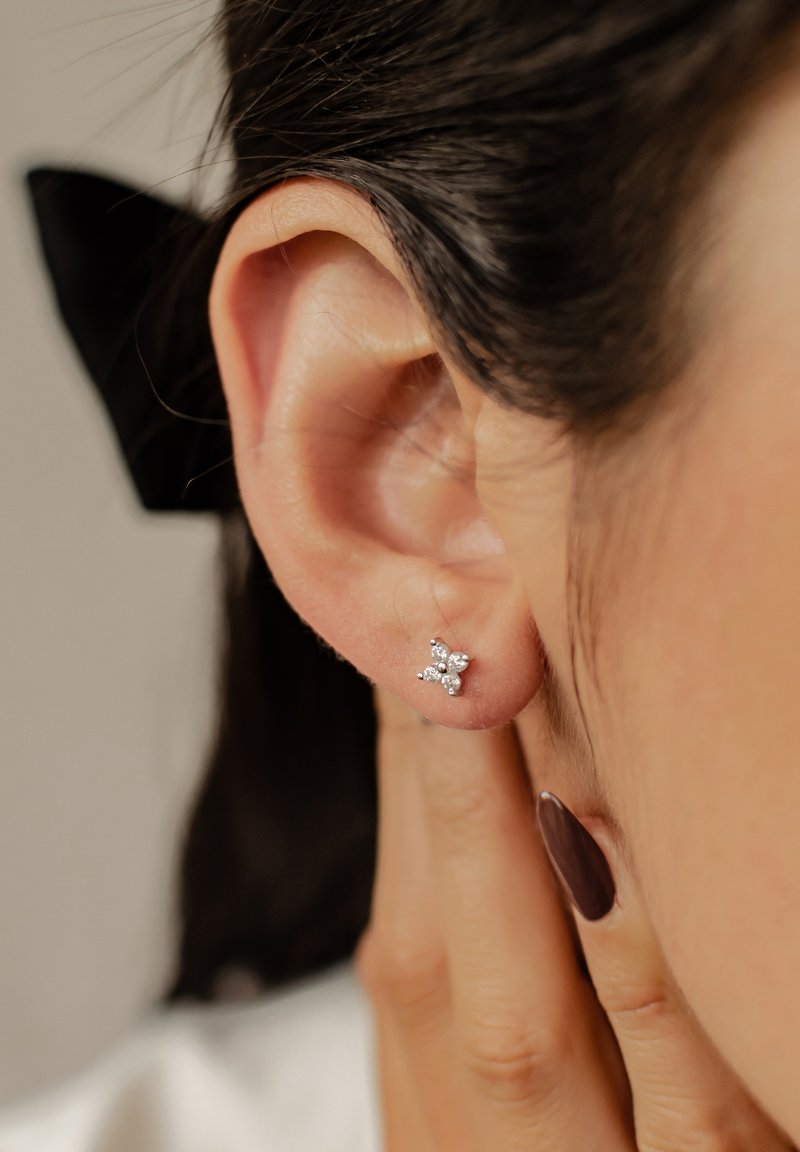 Orecchino a bottone in argento a forma di stella, adornato con piccole pietre preziose trasparenti. Vista ravvicinata vicino a un orecchio, con capelli scuri sullo sfondo.