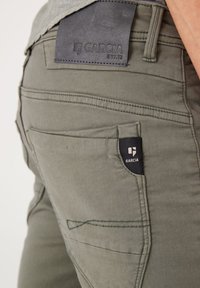 Pantalones casuales verdes hechos de una mezcla de algodón. Presentan una etiqueta negra en el bolsillo, detalles de costura sutiles y una textura suave.