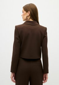 Brun cropped blazer med en spidse krave, glat stof, strukturerede skuldre og lange ærmer, parret med matchende bukser.