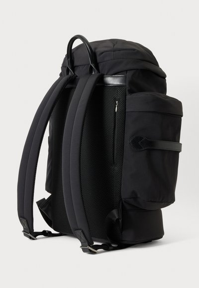 Sac à dos noir avec bretelles rembourrées, panneau arrière en mesh, poches latérales, poignée supérieure et une poche arrière zippée verticale, présenté sur un fond uni.