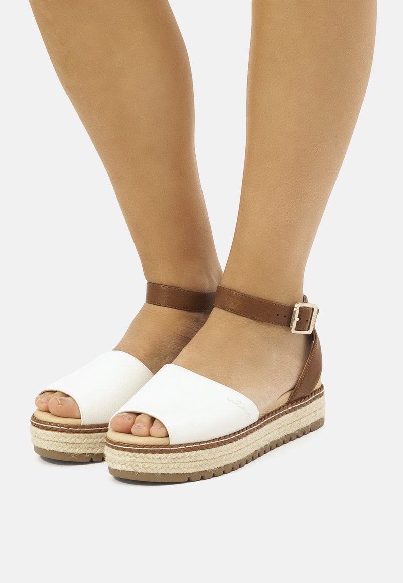 Sandalias de plataforma blancas de punta abierta con una correa en el tobillo marrón, que cuentan con una suela de yute trenzado, textura suave y un diseño minimalista.