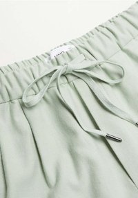 Shorts à taille élastique vert clair avec un cordon de serrage et des embouts métalliques argentés. Le tissu présente une finition lisse et texturée.
