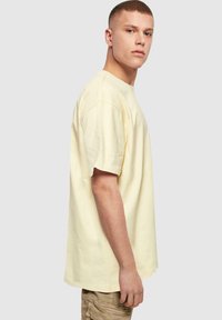 Gul bomulds T-shirt med afslappet pasform, korte ærmer og synlige syninger. Simpel rund halsudskæring.