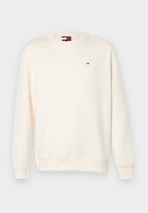 Sweter w kolorze kremowym, wykonany z miękkiego materiału, z długimi rękawami, okrągłym dekoltem oraz małym logo na klatce piersiowej.