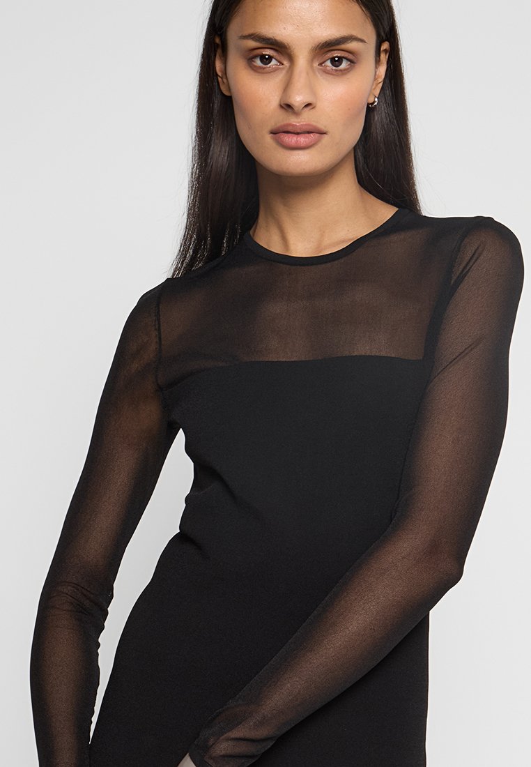 Haut noir à manches longues avec un panneau supérieur en tulle transparent et un corps ajusté, fabriqué en tissu extensible pour le confort et la liberté de mouvement.