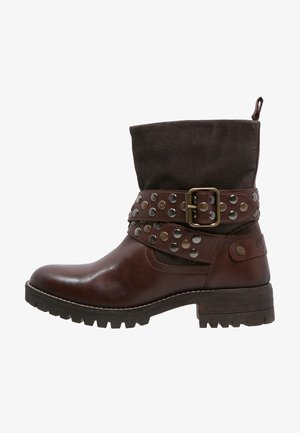 Botte en cuir brun jusqu'à la cheville avec un revers en tissu brun foncé. Caractéristiques d'une boucle et de clous en métal sur la sangle. Semelle en caoutchouc épaisse.
