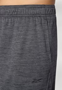 Calças de desporto cinzentas com um tecido texturizado, cintura elástica e um bolso lateral. Apresenta um logotipo preto perto da bainha.