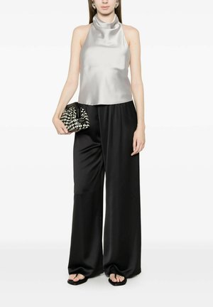 Donna che indossa una maglia smanicata in raso argento, pantaloni neri in raso a gamba larga, sandali neri e tiene una pochette con motivo bianco e nero.